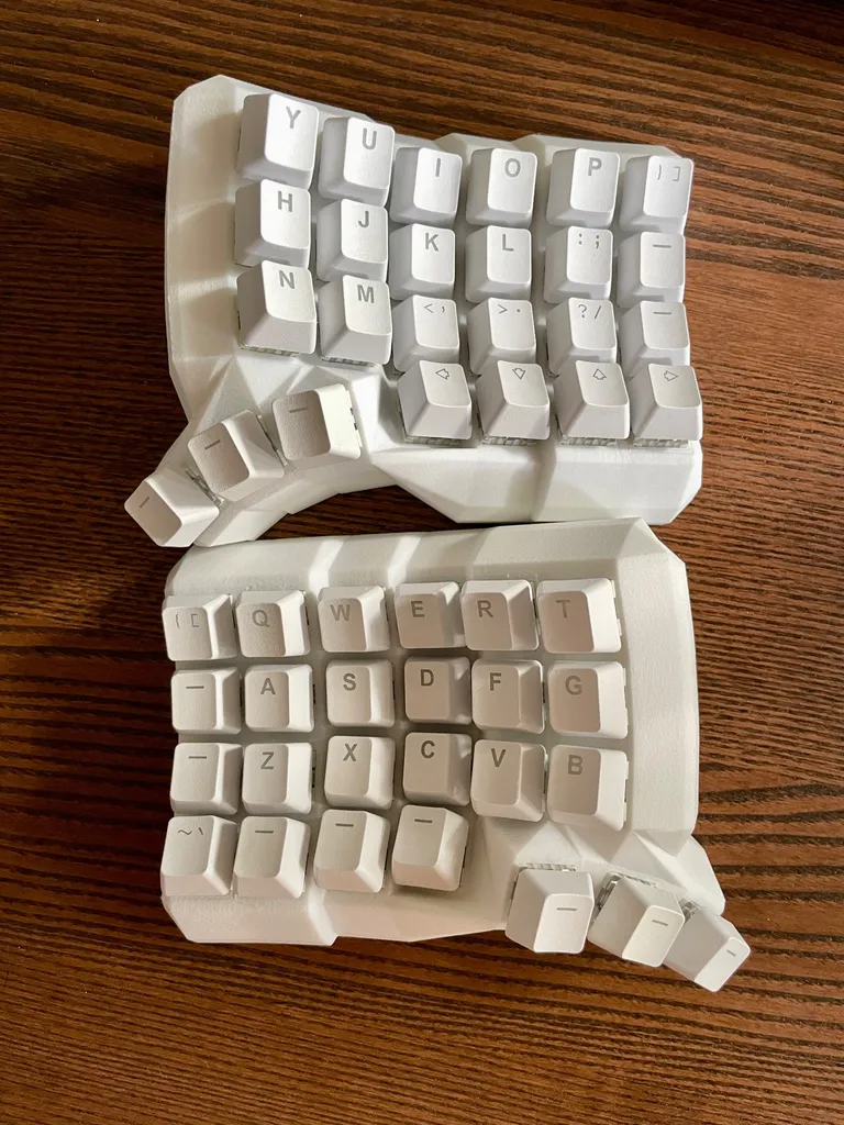 Both halves of the rebuilt Dactyl Manuform in white nylon, white caps on, on my desk