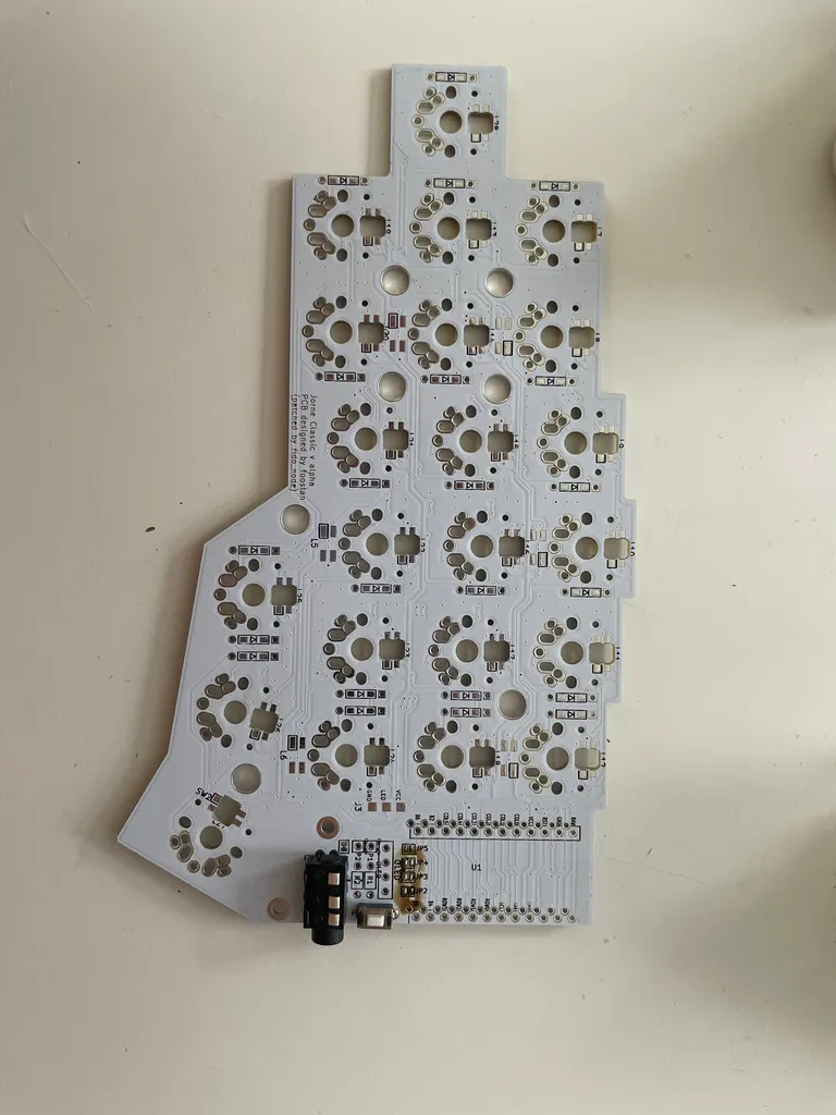 One bare white Corne PCB back from JLCPCB, with the TRRS jack and reset switch still loose